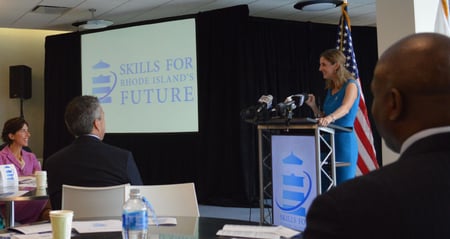 Woman speaking at podium with Skills for Rhode Island's Future logo