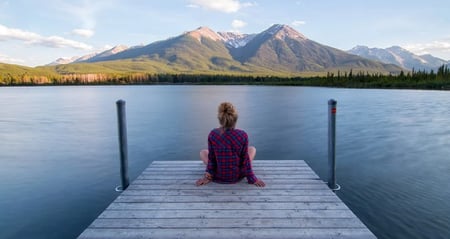 woman relaxing on dock at lake with mountains in the background